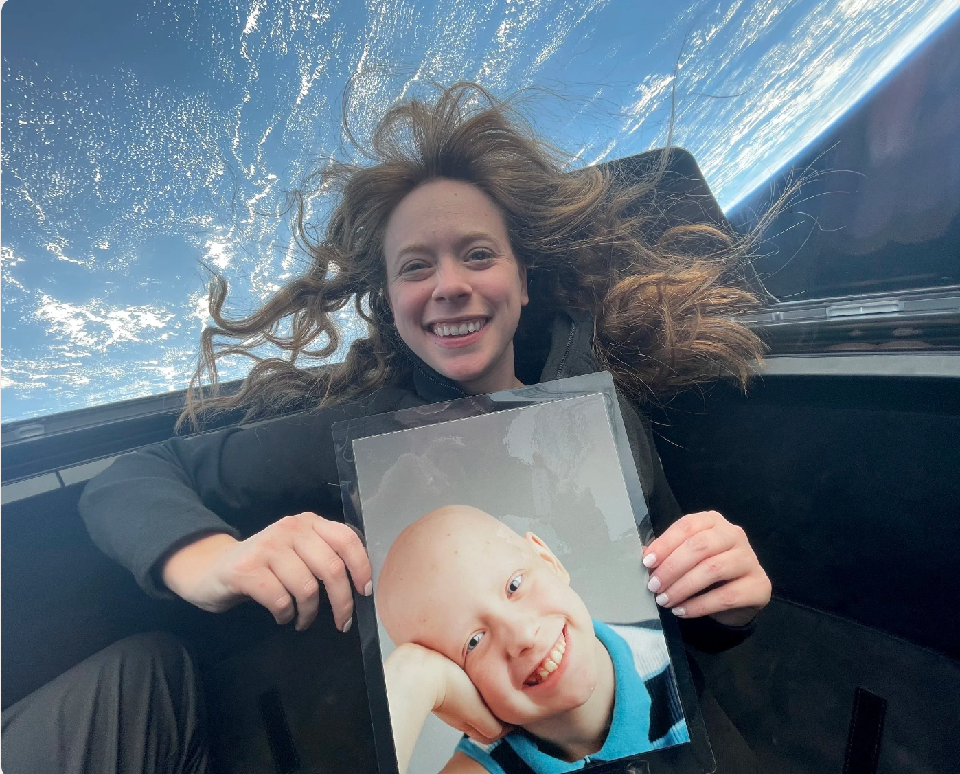 Hayley Arceneaux smiling in zero gravity, holding a photograph from her childhood cancer treatment at St. Jude.